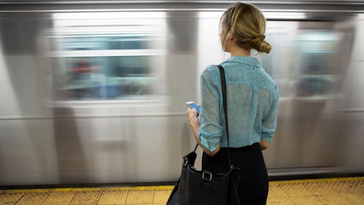 a woman standing in front of a train with her back to the camera and holding a cell phone