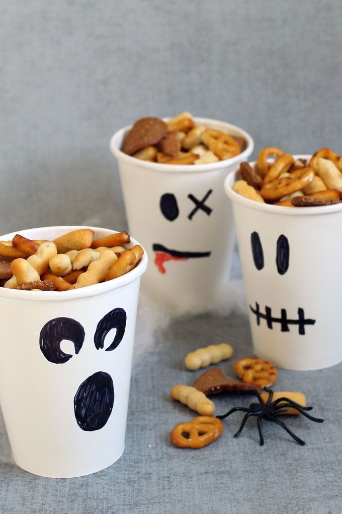 three white cups filled with halloween treats on top of a table