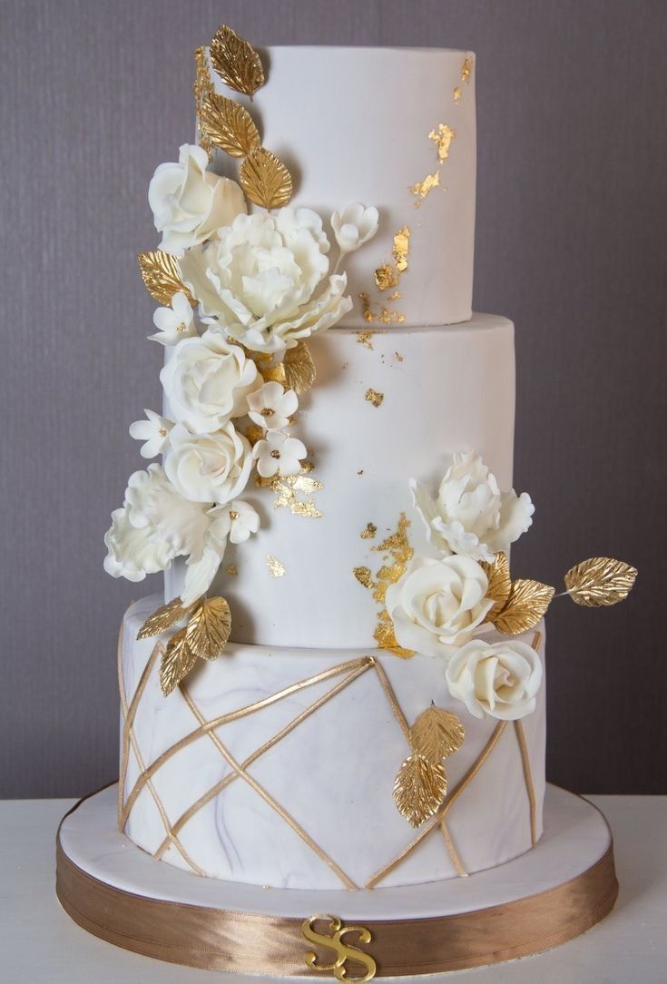 a white and gold wedding cake with flowers on top