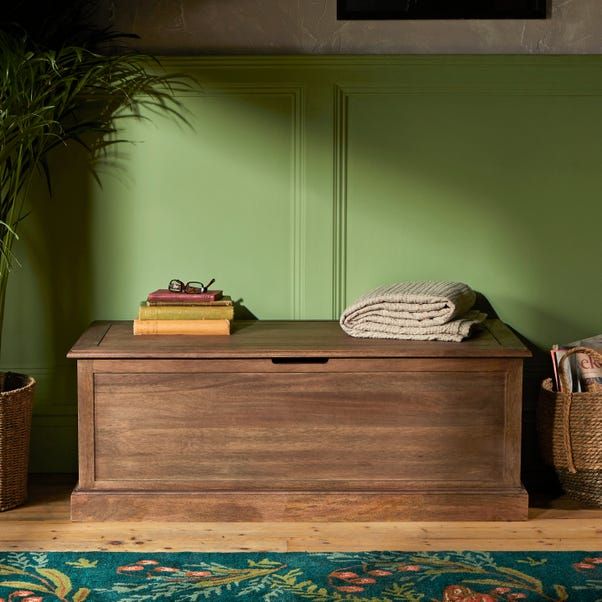 a wooden trunk sitting on top of a rug next to a potted plant