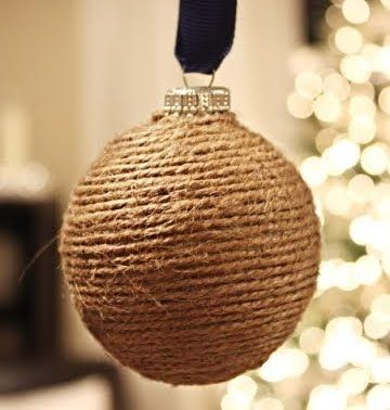 a ball ornament hanging from a rope with a blue ribbon on it and a christmas tree in the background