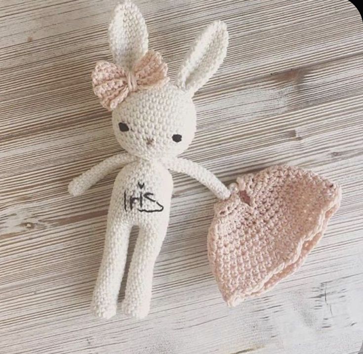 a crocheted bunny doll next to a knitted hat on a wooden surface