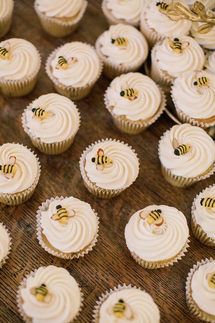 cupcakes with white frosting and bees on them sitting on a wooden table