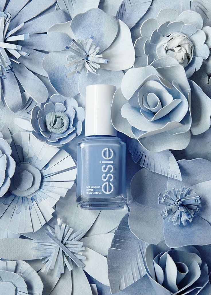 a bottle of essie nail polish sitting on top of blue and white paper flowers