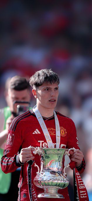 a young man holding a silver cup in his hands and wearing a red shirt with the manchester united crest on it