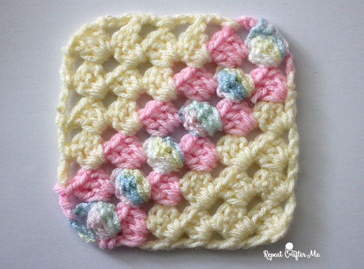 a crocheted square is shown on a white surface with pink and blue flowers