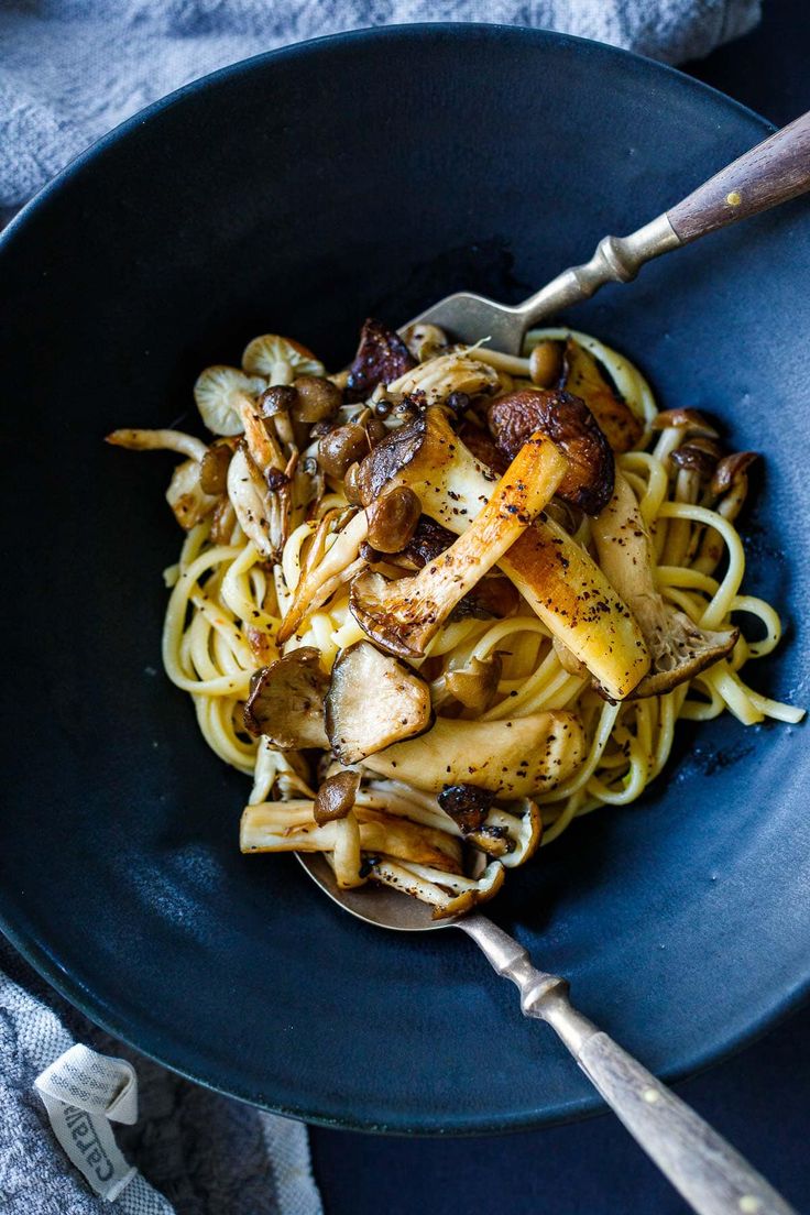 a bowl filled with pasta and mushrooms on top of a blue plate next to a wooden spoon