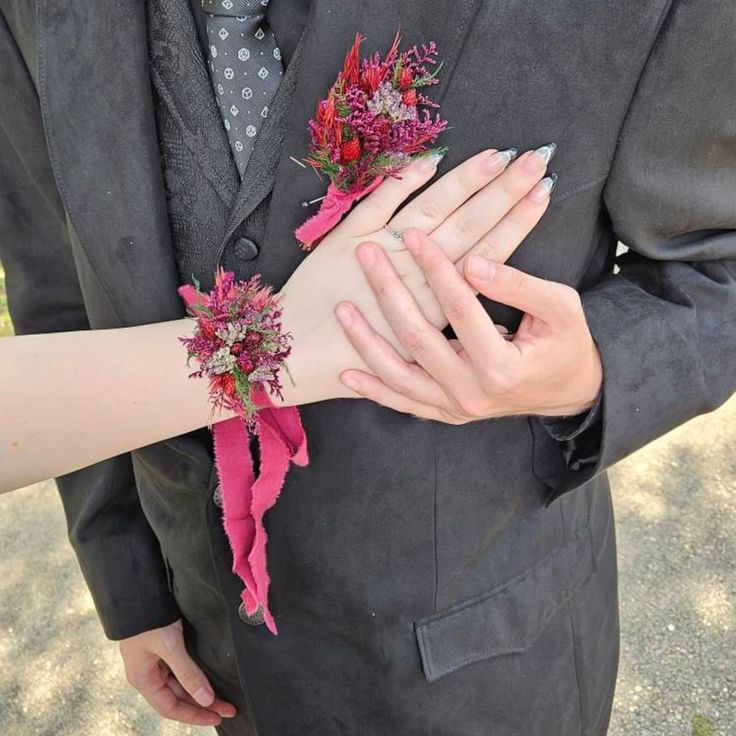 a man in a suit and tie with flowers on his arm holding another woman's hand