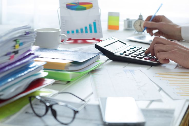 two people working at a desk with papers, calculator and glasses on it