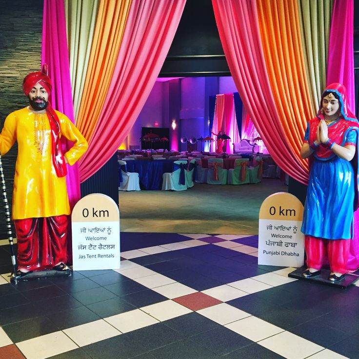 two colorfully dressed statues stand next to each other in front of a stage decorated with drapes