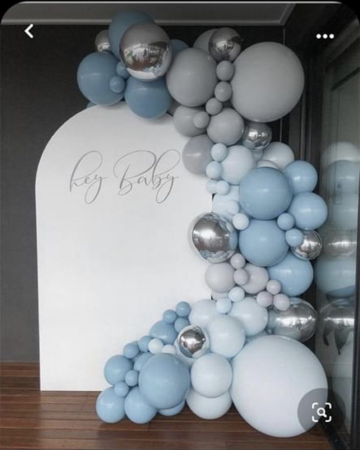 an arch made out of balloons and silver balls is displayed in front of a baby's name sign