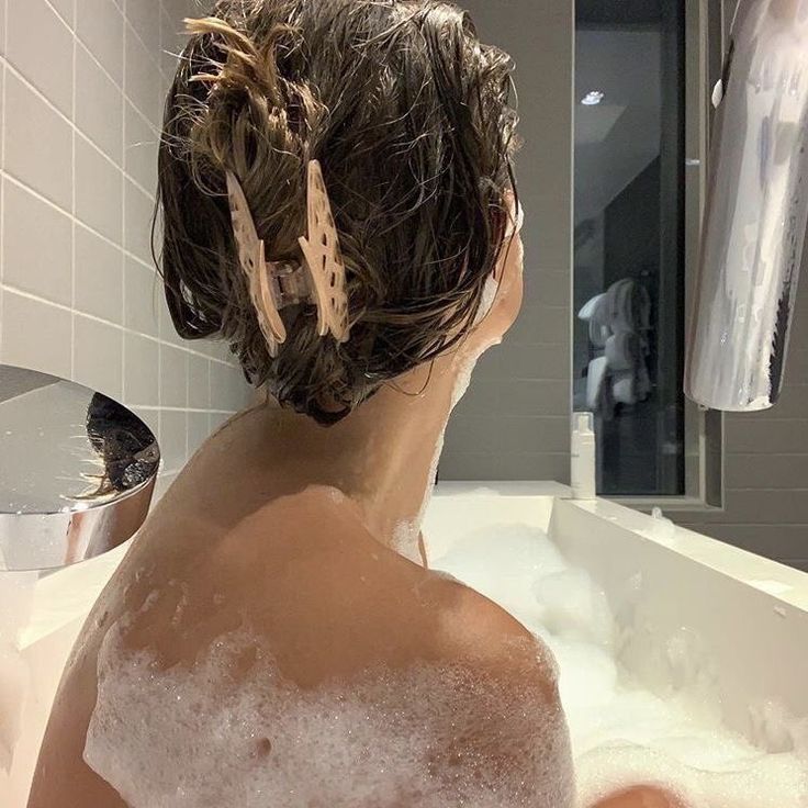 a woman is sitting in the bathtub with foam on her head and hair pulled back