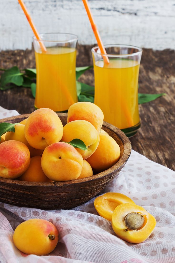 a wooden bowl filled with peaches next to two glasses of orange juice