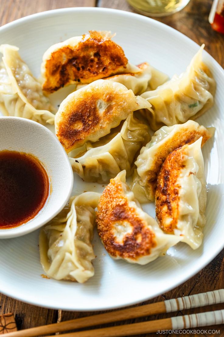 some dumplings are sitting on a plate with dipping sauce next to chopsticks