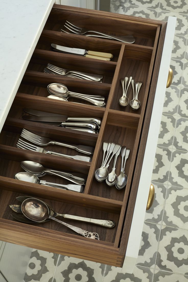 an open drawer with silverware and spoons in it on a tiled floor next to a wall