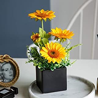 a vase with yellow flowers on a white table next to an old photo and other items