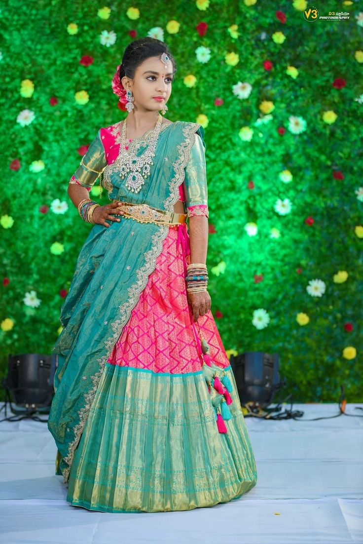 a woman in a blue and pink lehenga with flowers on the wall behind her