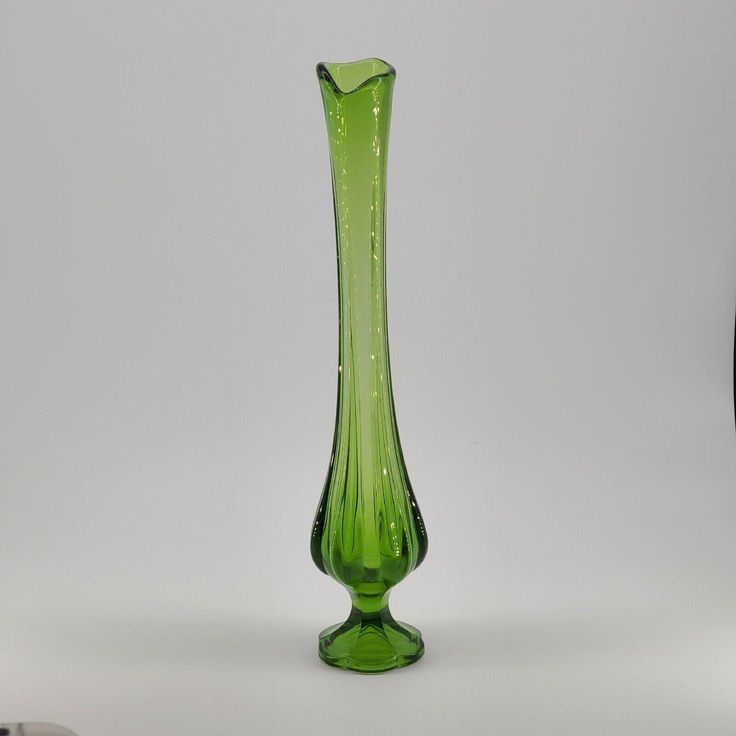 a green glass vase sitting on top of a white table next to a black object