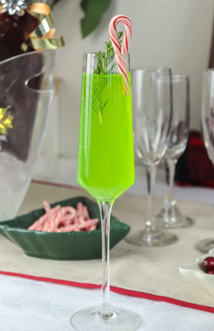 a green drink with candy canes in it sitting on a table next to other glasses