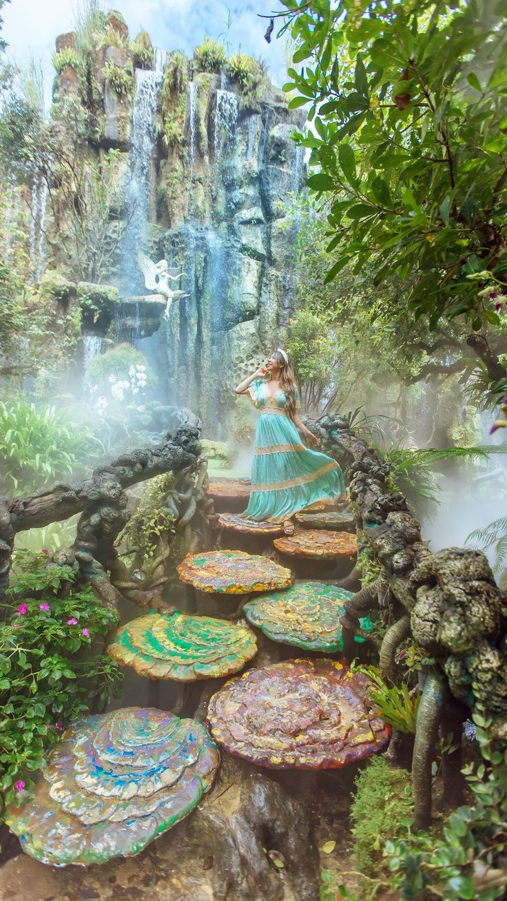 a woman in a blue dress standing on a rock path surrounded by water lilies