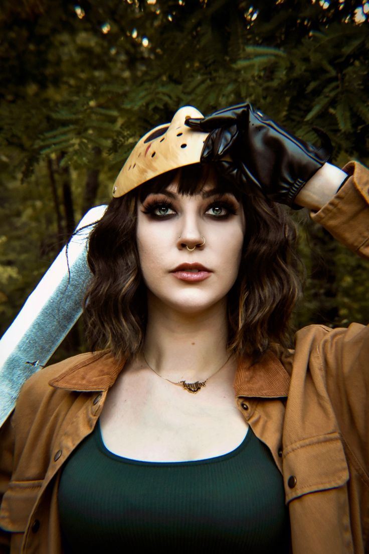 a woman wearing a helmet and holding a knife over her head with trees in the background