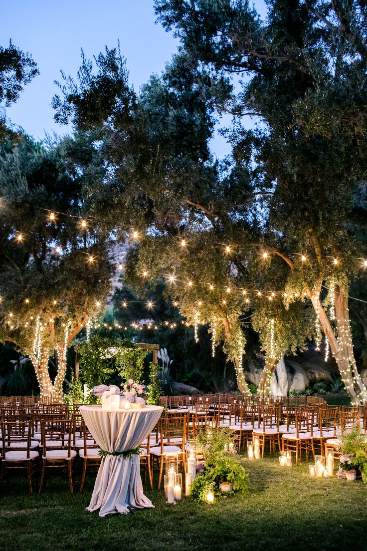 an outdoor wedding venue with tables and chairs set up for dinner under the trees at night