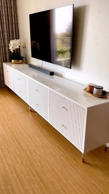 a flat screen tv sitting on top of a white cabinet in front of a window