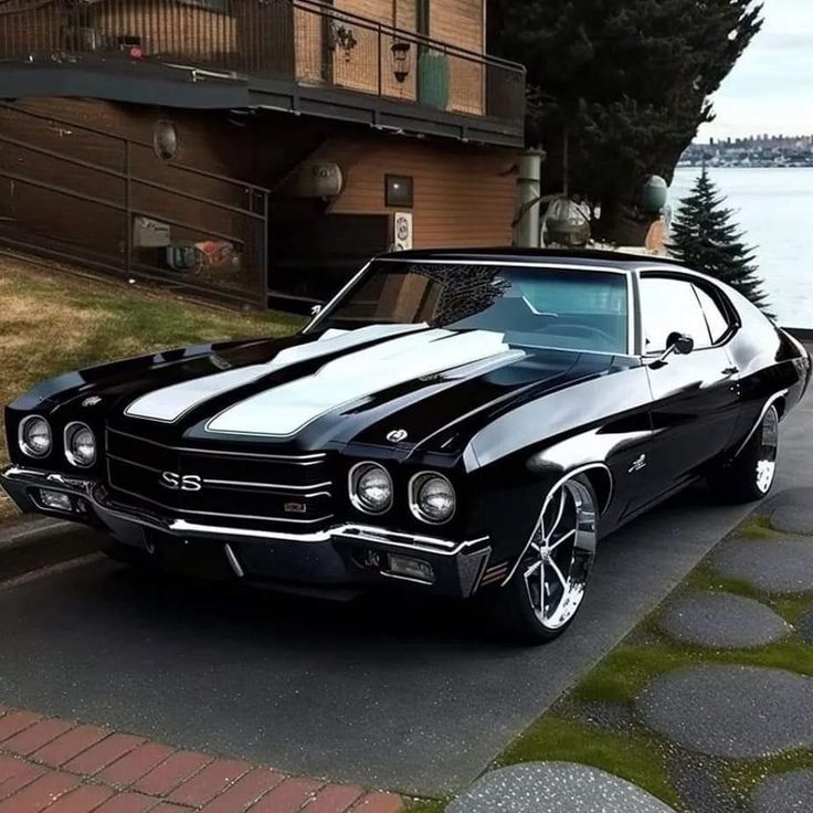 a black and white muscle car parked on the side of the road next to water