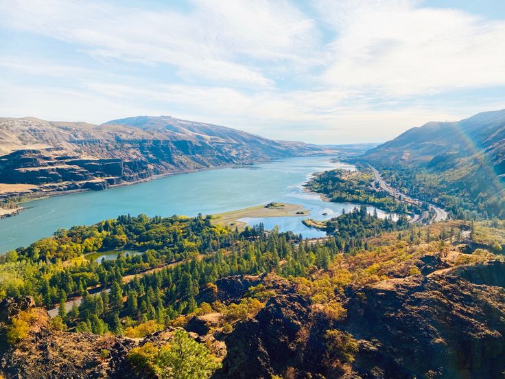 an aerial view of a lake surrounded by mountains and trees in the foreground with sun shining on the water