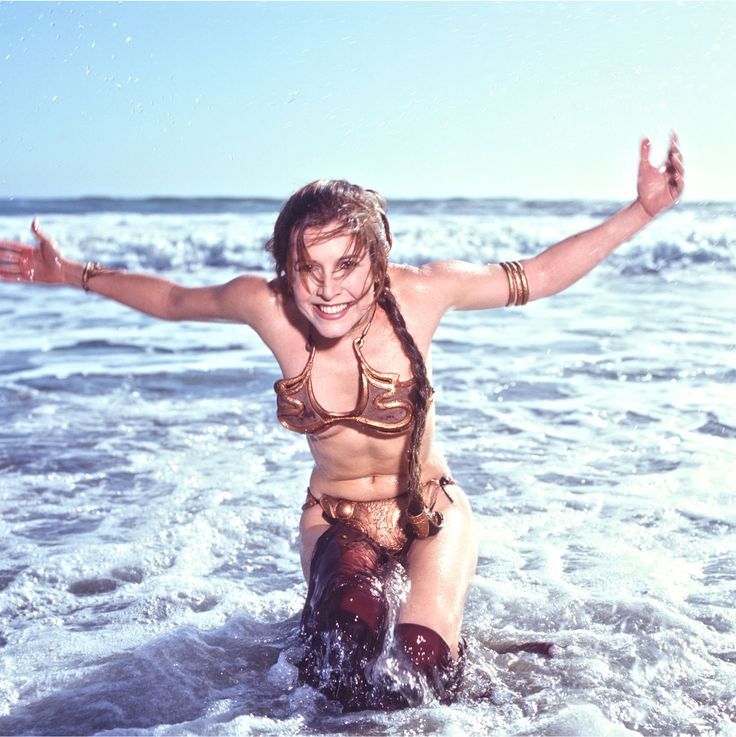 a woman in a bathing suit sitting on the beach with her arms outstretched and legs spread out