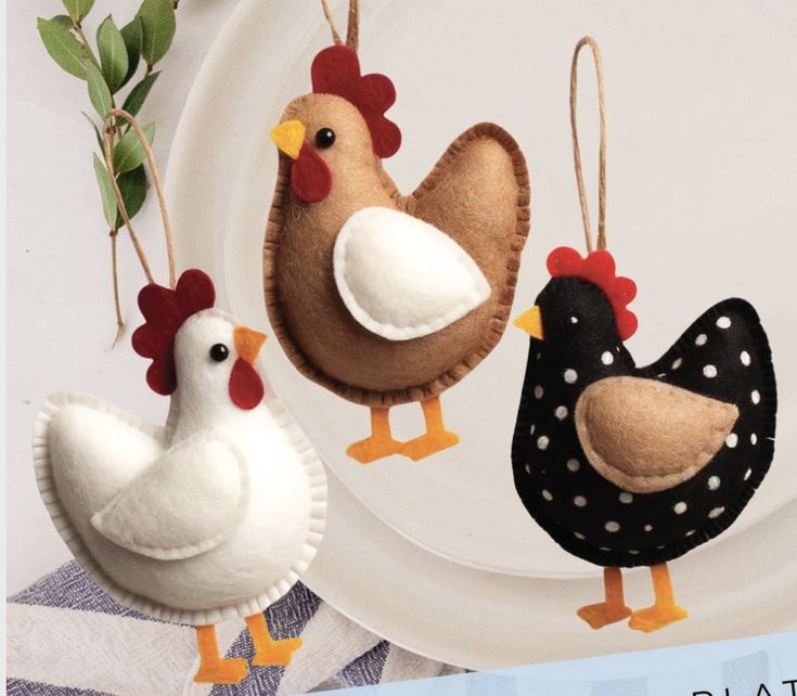 three felt chickens hanging from strings on a plate