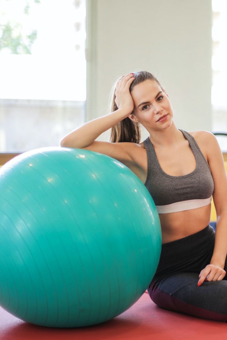 a woman sitting on the floor next to an exercise ball and holding her hand near her head