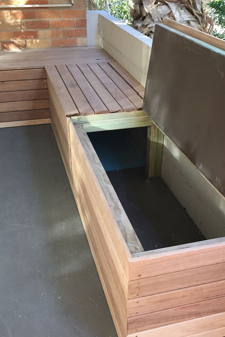 a wooden bench sitting on top of a cement floor next to a tree and bushes