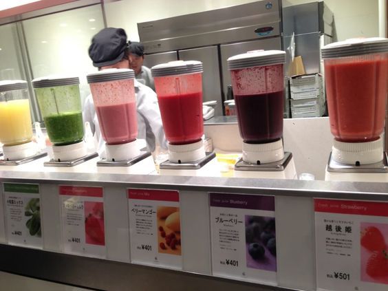 there are many different types of juices on the counter at this restaurant, and one person is working in the background