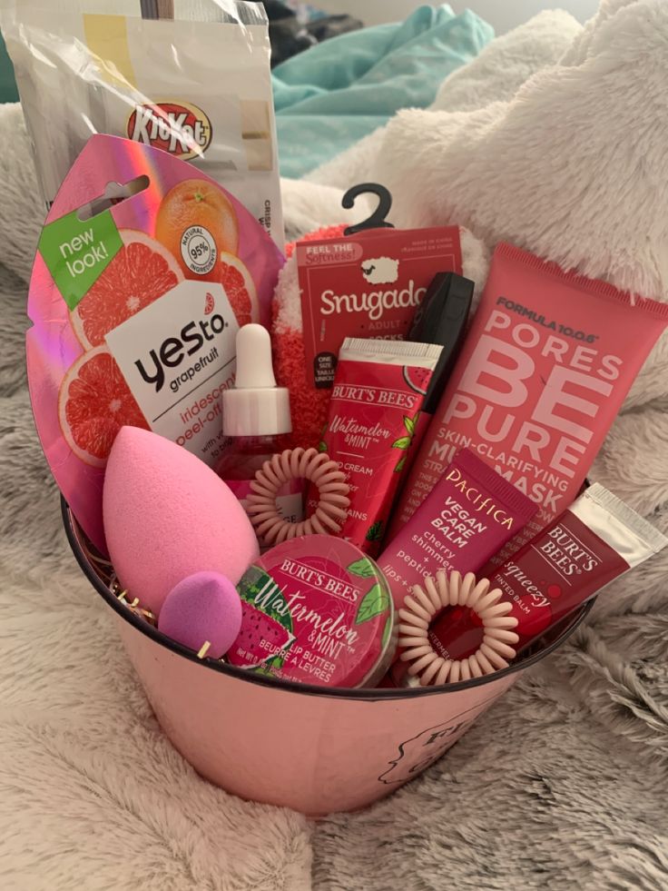 a pink bowl filled with lots of different items on top of a white blanket next to a teddy bear