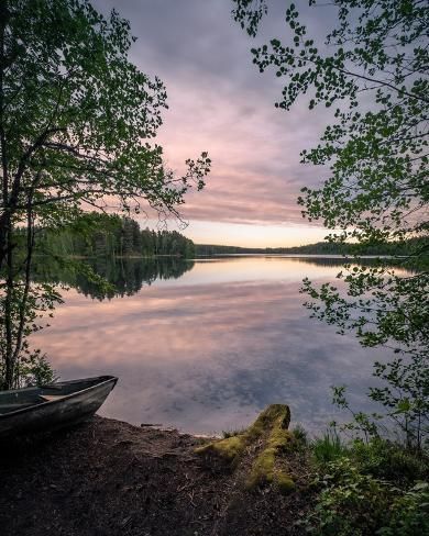 a canoe is sitting on the shore of a lake at sunset with trees in the foreground