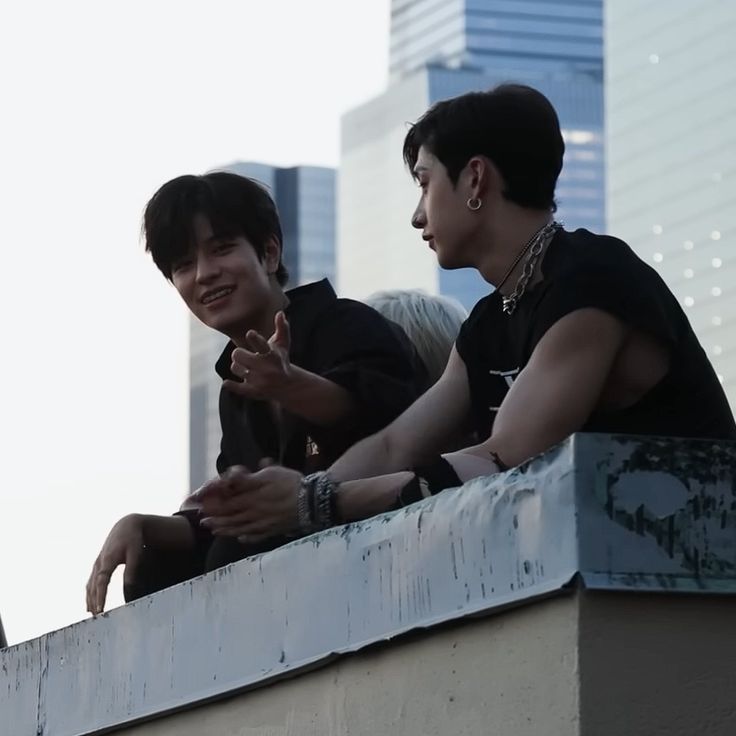 two young men sitting next to each other on top of a building near tall buildings