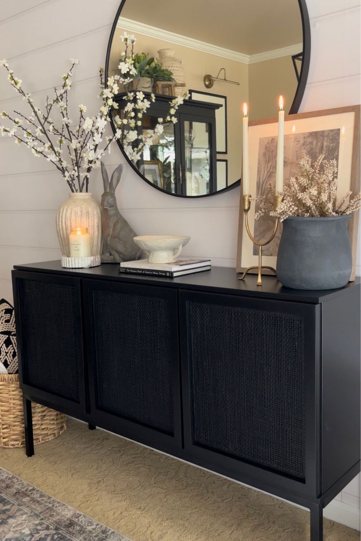 a living room with a large round mirror on the wall and a black sideboard