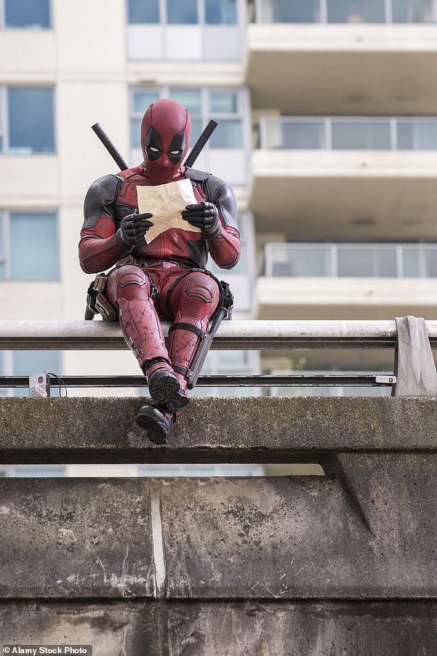 a deadpool is sitting on a ledge reading a piece of paper