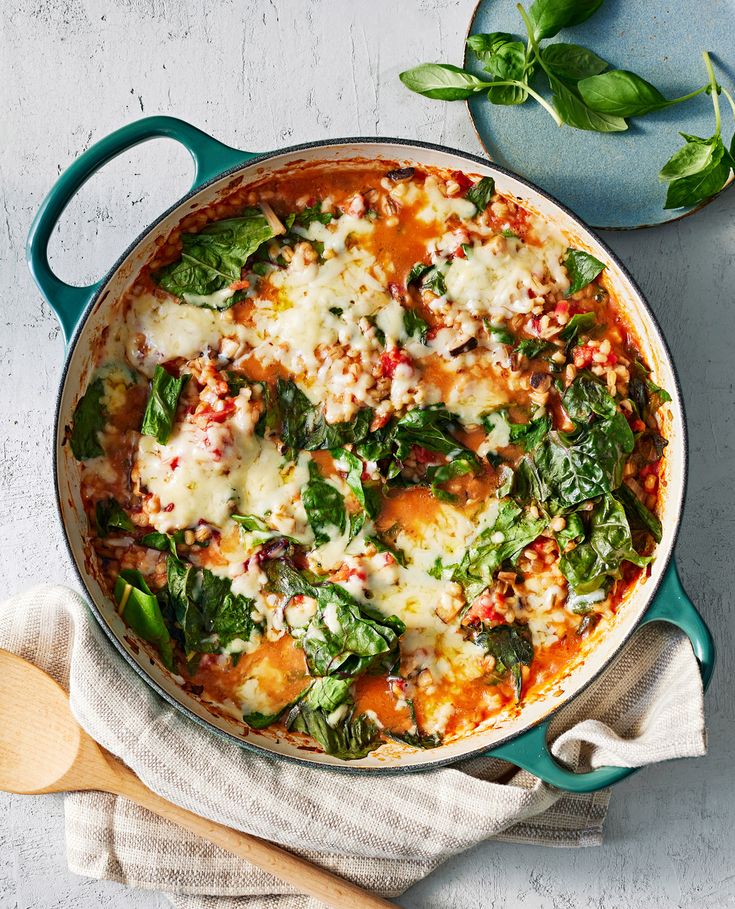 a blue pot filled with spinach and cheese on top of a white table next to a wooden spoon