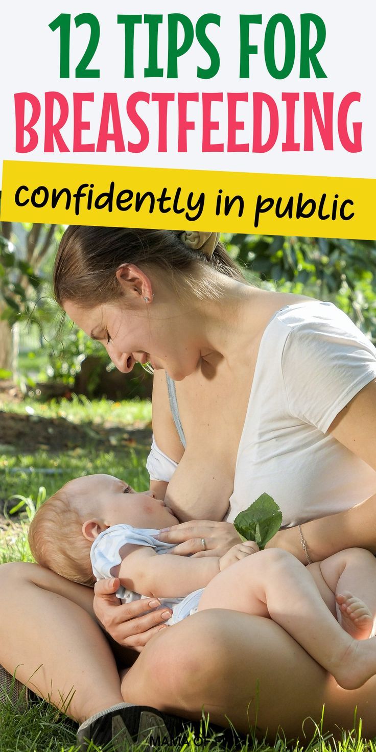 a woman breastfeeding her baby while sitting on the grass with trees in the background