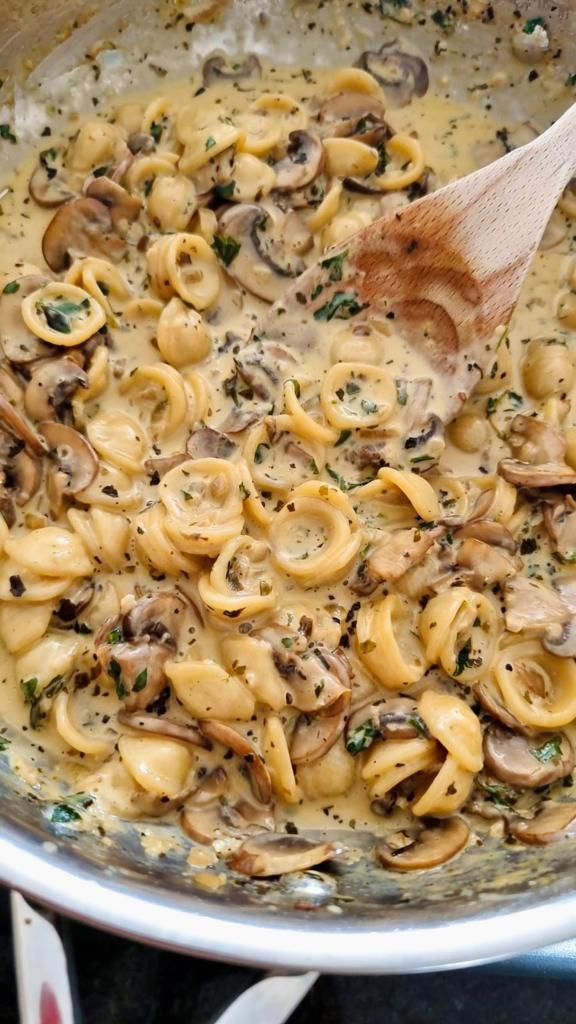 a wooden spoon in a pot filled with pasta and mushrooms