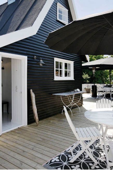 an outdoor deck with chairs and umbrellas next to a black wooden house that has white trim on it