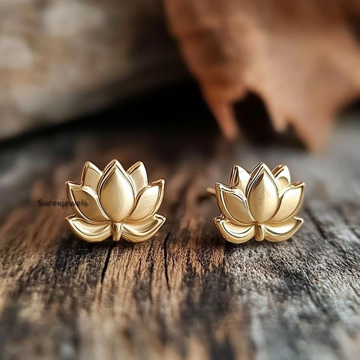 two gold lotus stud earrings sitting on top of a wooden table