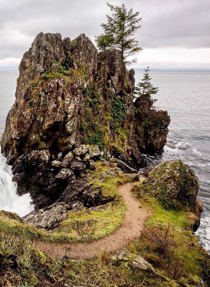 a man sitting on top of a cliff next to the ocean with a waterfall coming out of it