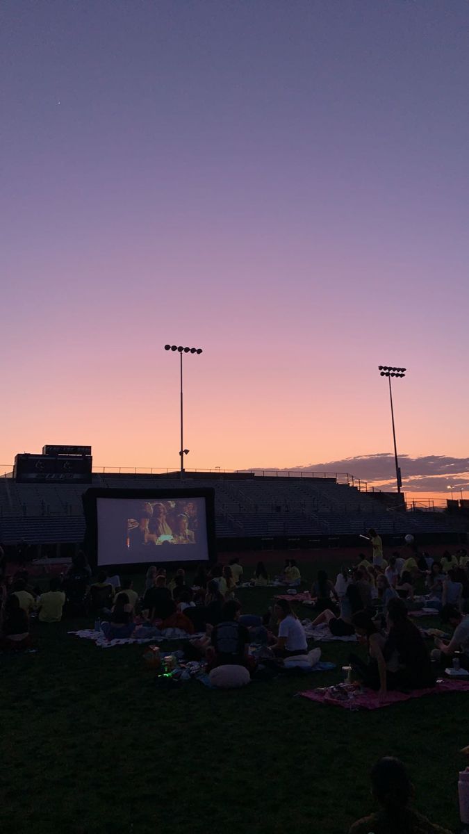 people are sitting on the grass watching movies at sunset or dawn in an empty stadium