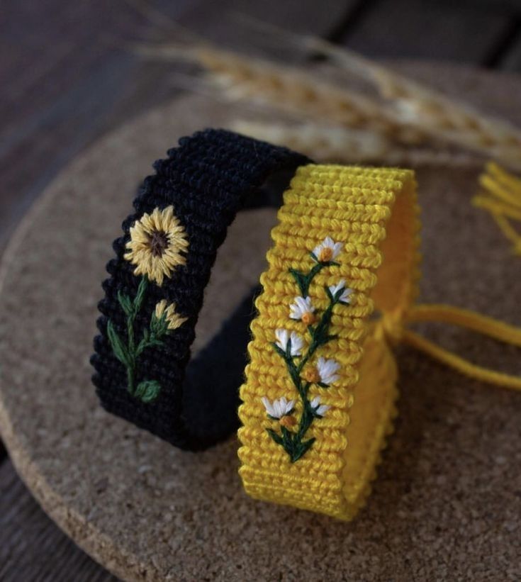 two crocheted bracelets with flowers on them sitting on a wooden table next to each other