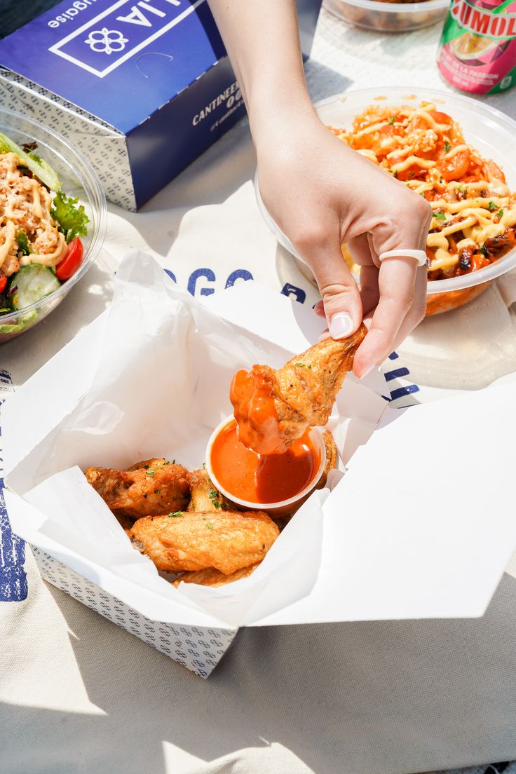 a person dipping some food into a container on a table with other foods and drinks