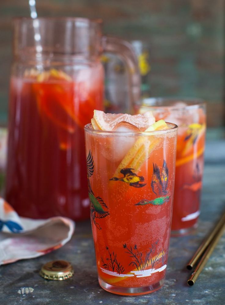 two glasses filled with red liquid sitting on top of a table next to silverware