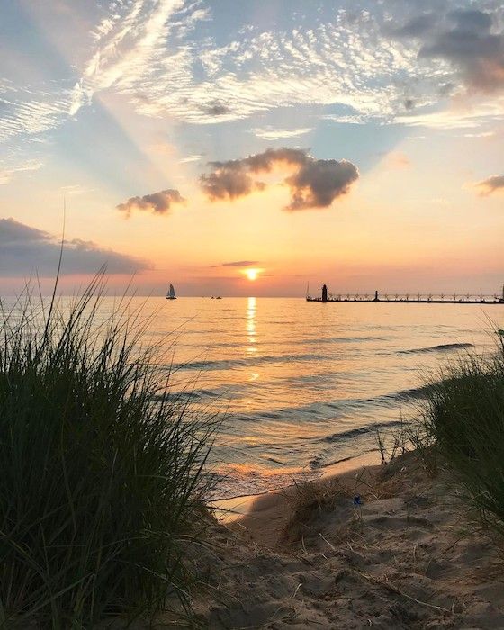 the sun is setting over the ocean with sailboats in the water and tall grass